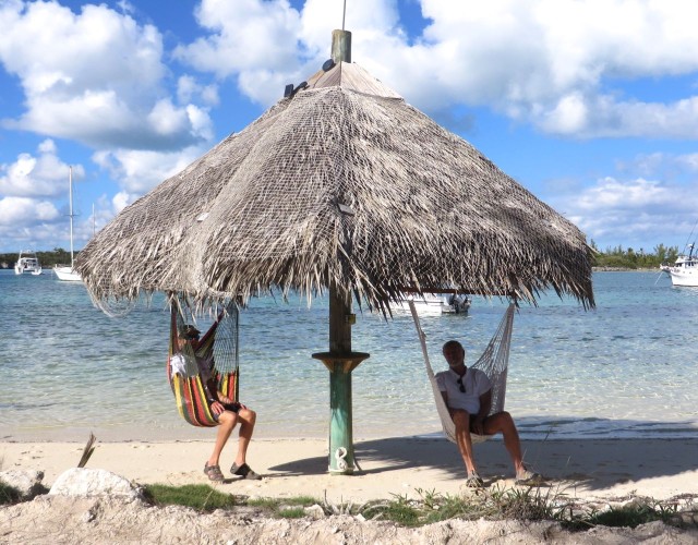 The guys are hanging out in  swinging chair hammocks under a tiki style roof.