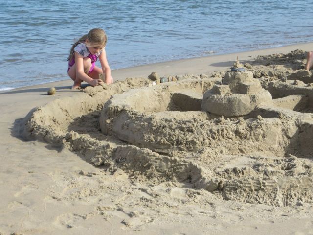 A little girl working on her sand fort.