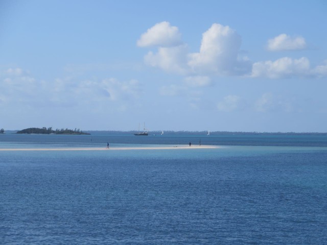 In the distance, over the sandbar beach, is a two-masted schooner.